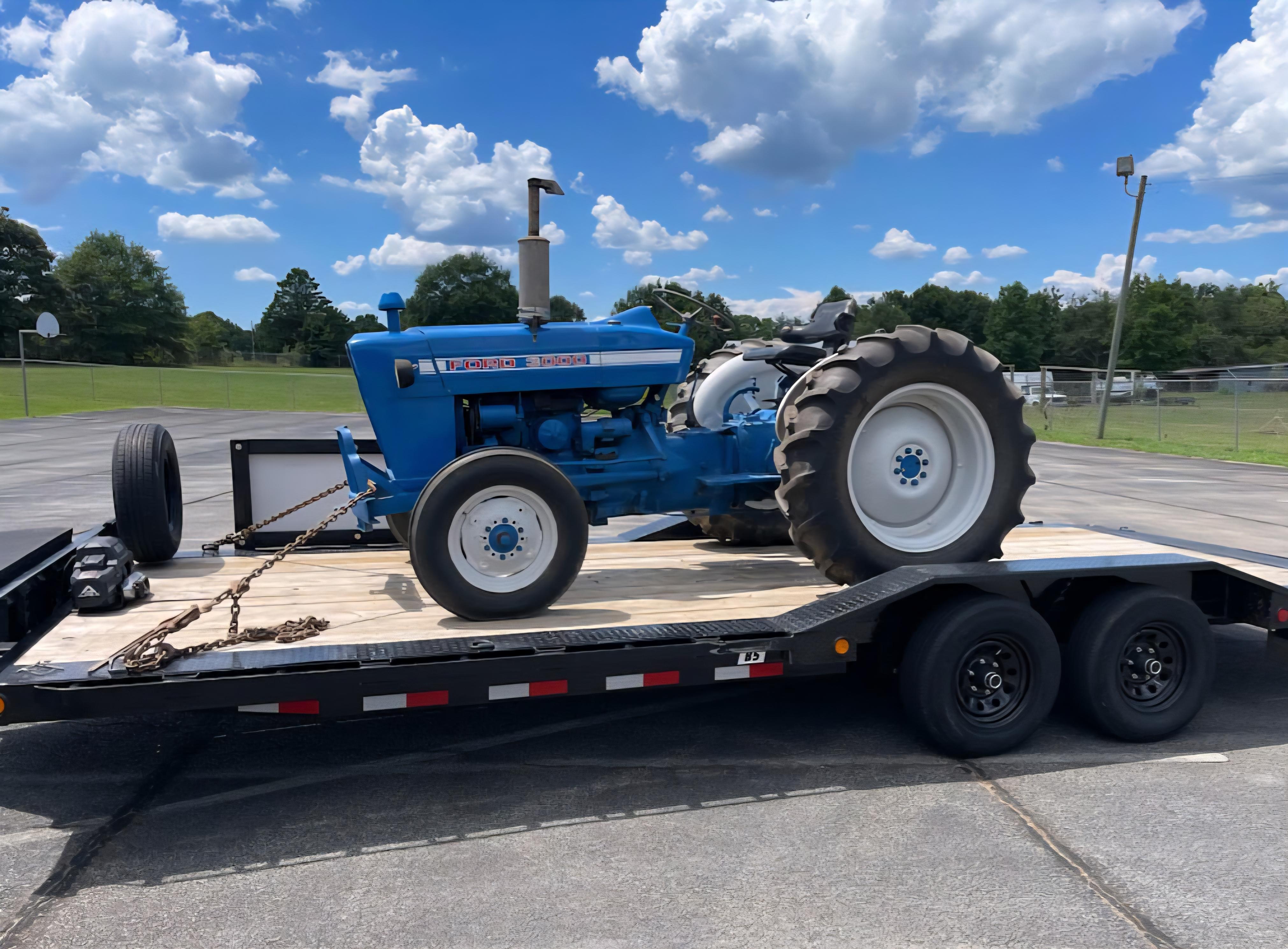 Blue Ford 3000 tractor loaded on a flatbed trailer under blue skies