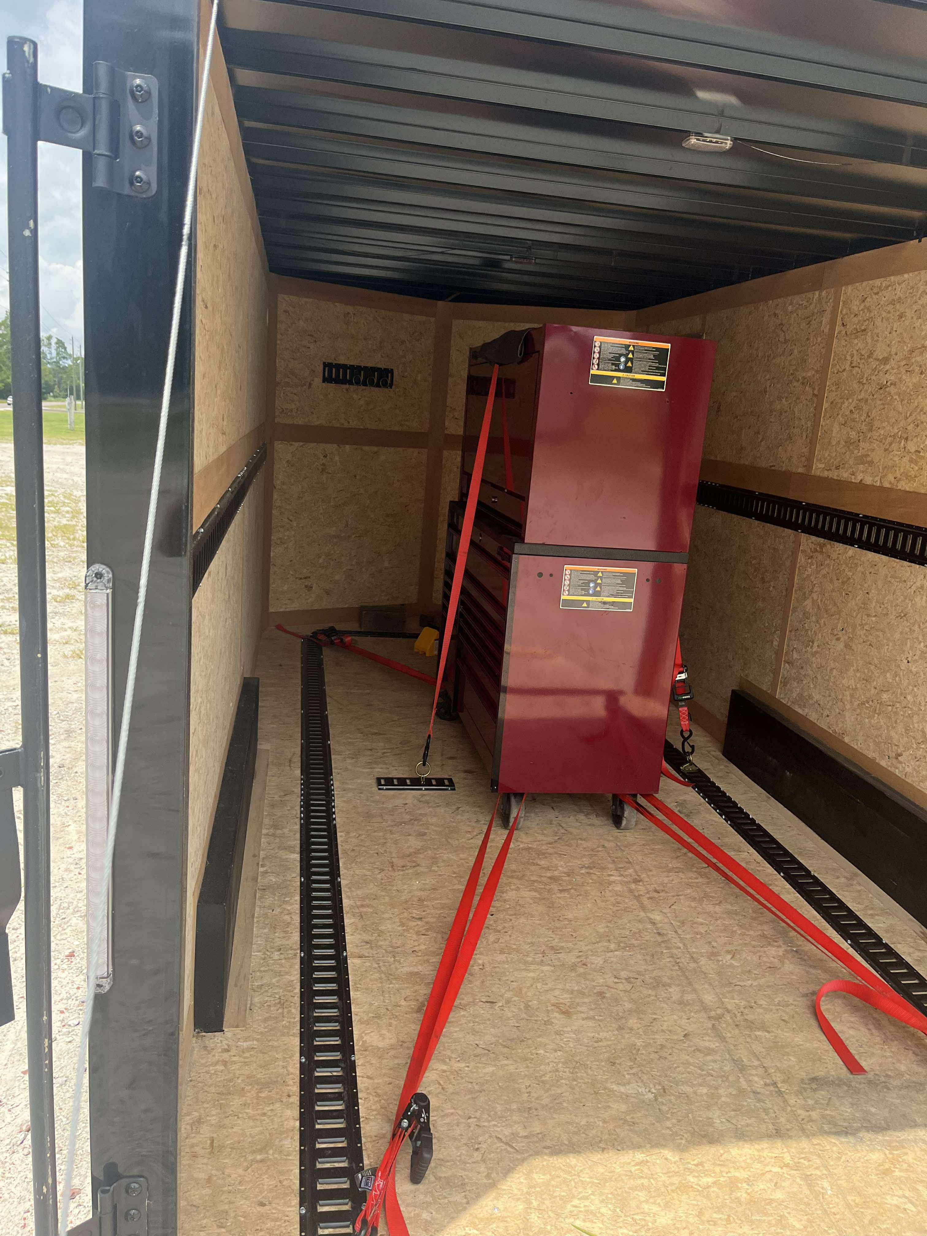 Enclosed trailer interior with red toolbox secured with tie-down straps