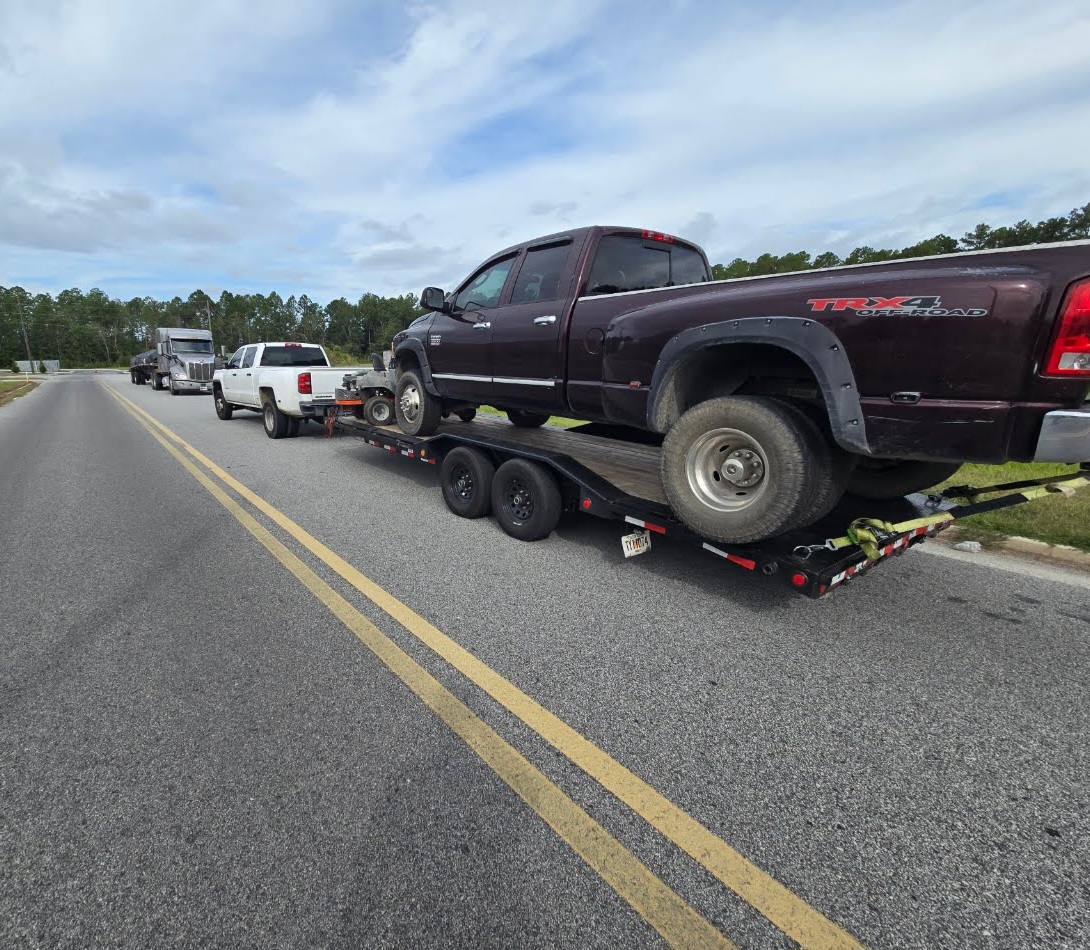 Flatbed trailer transporting a large Ram dually truck on highway