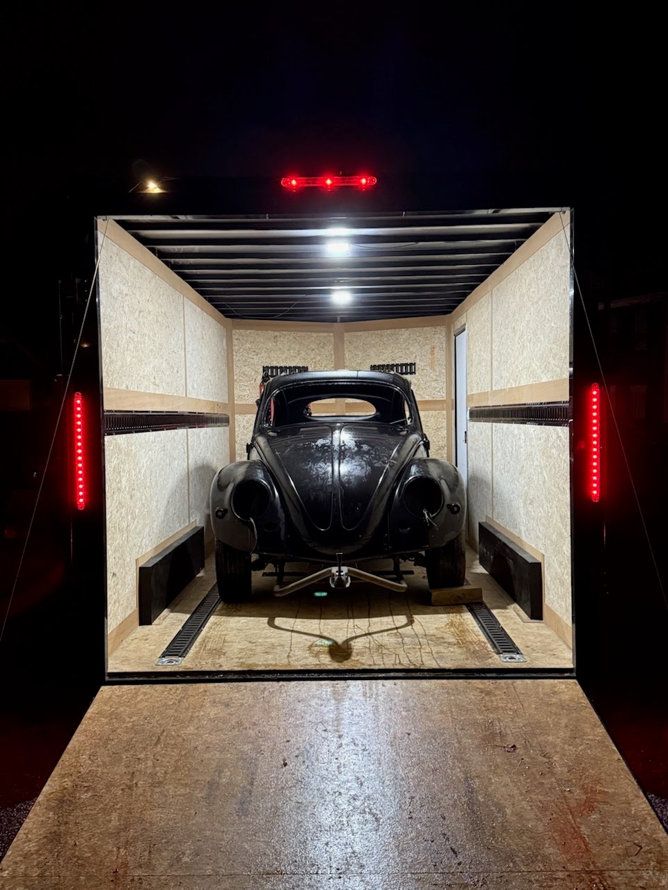 Black classic Volkswagen Beetle inside an enclosed trailer at night