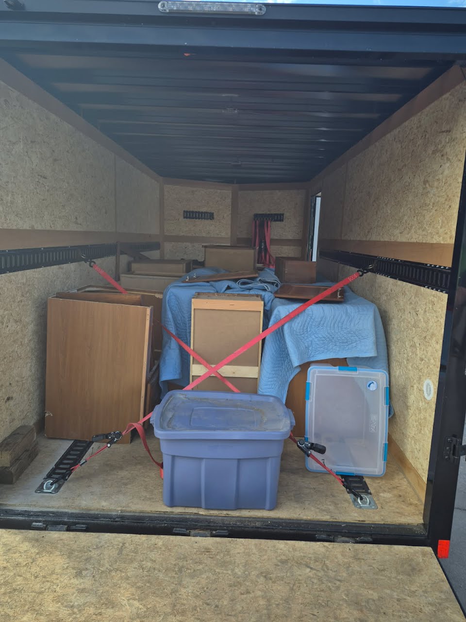 Furniture, cabinets, and moving totes strapped inside an enclosed cargo trailer