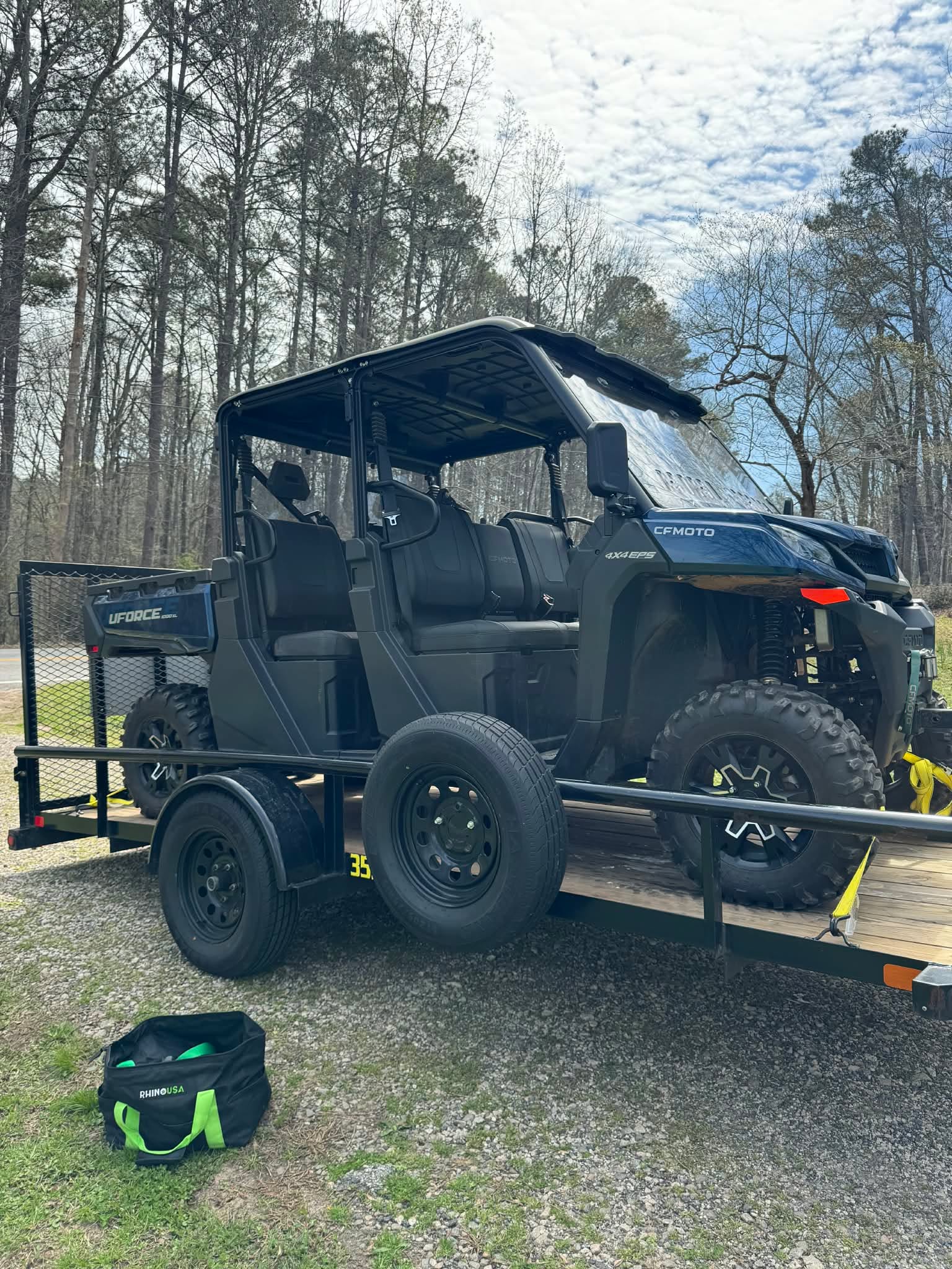 Blue CFMoto UForce 4x4 side-by-side on a utility trailer in a wooded area