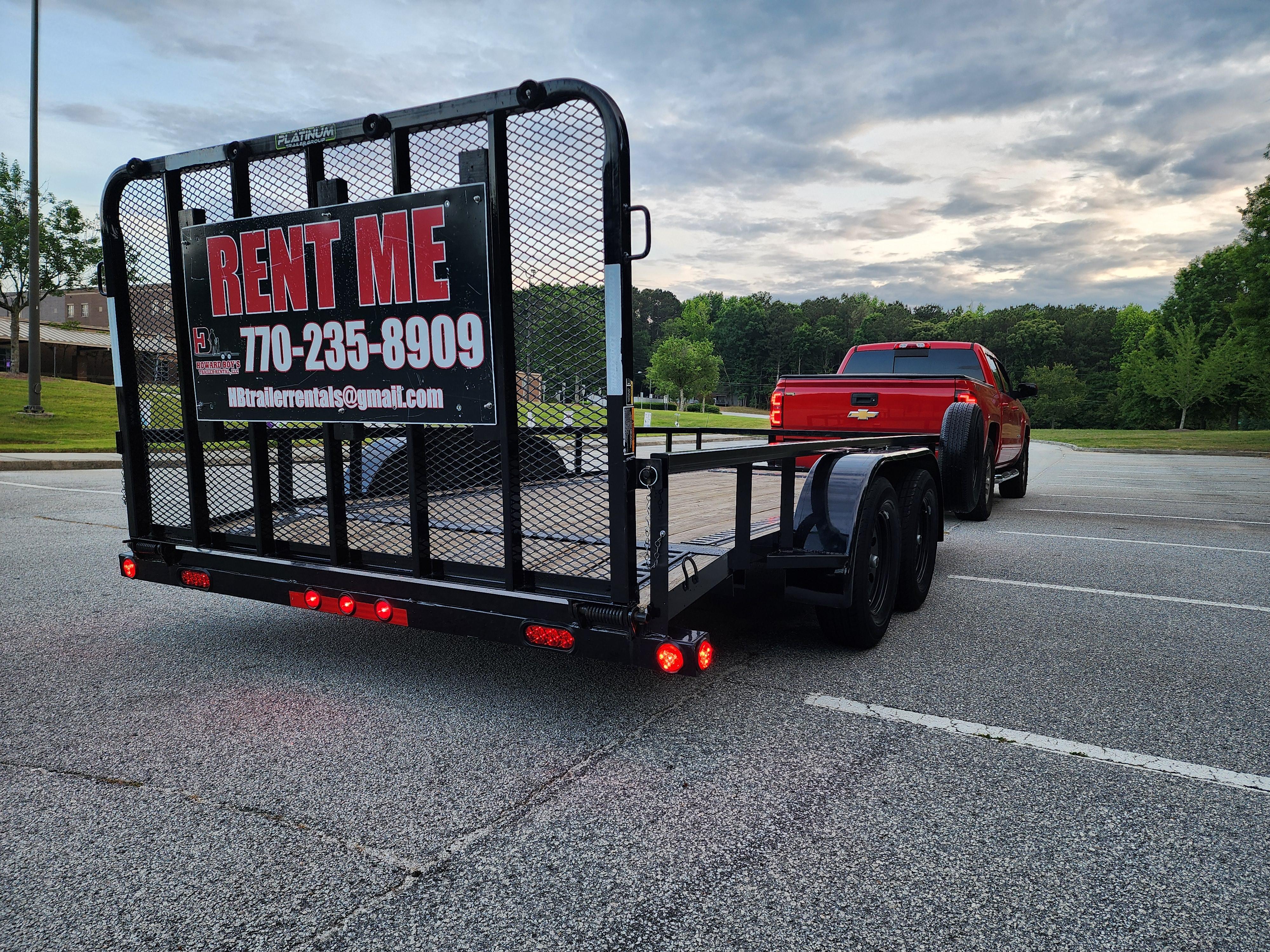 Rear view of a Howard Boys Rent Me utility trailer towed by a red Chevy truck