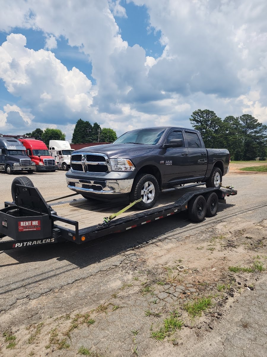 Flatbed trailer hauling a gray Ram 1500 pickup truck