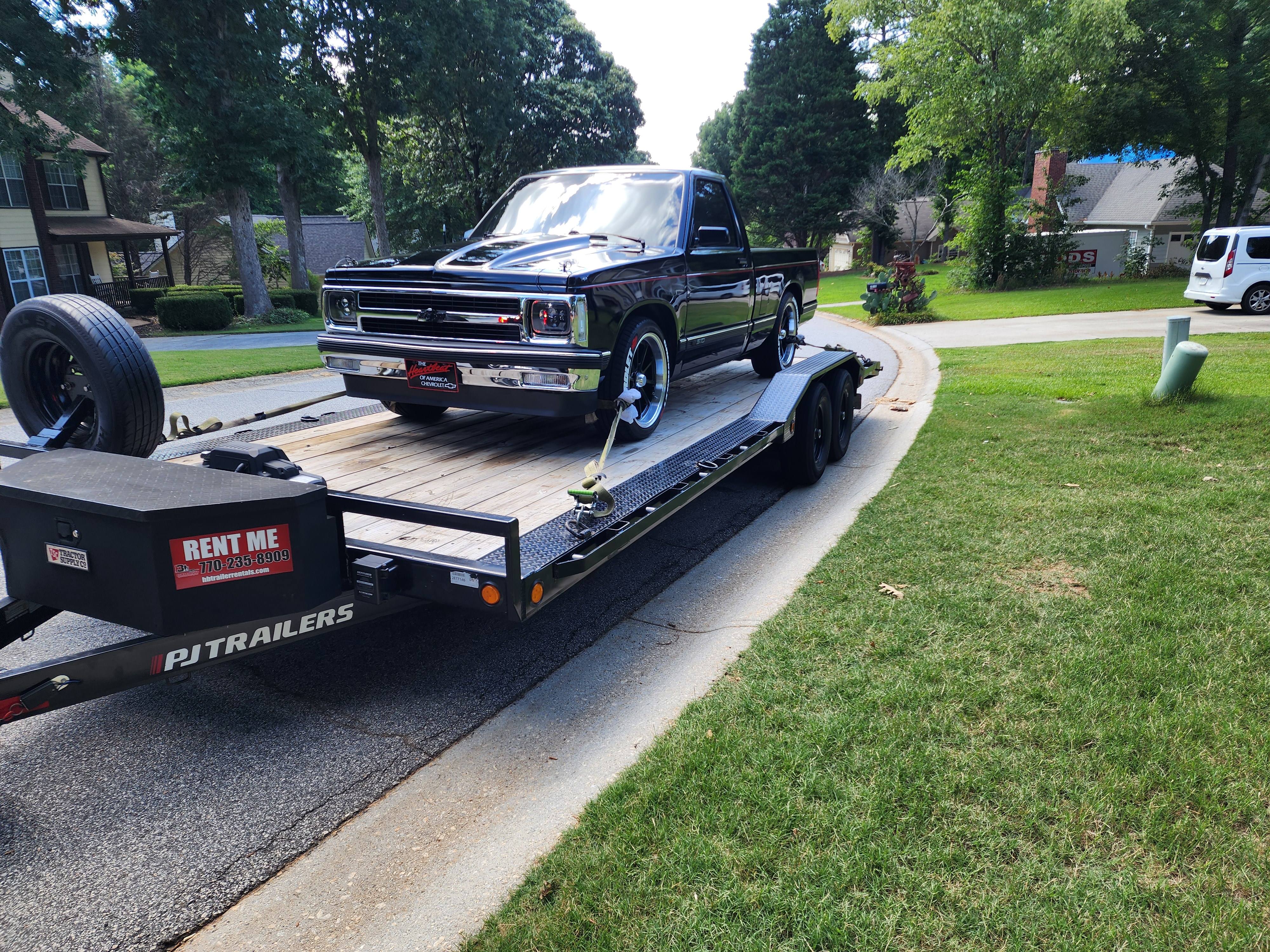 Flatbed car hauler carrying a black classic Chevy S10 pickup truck
