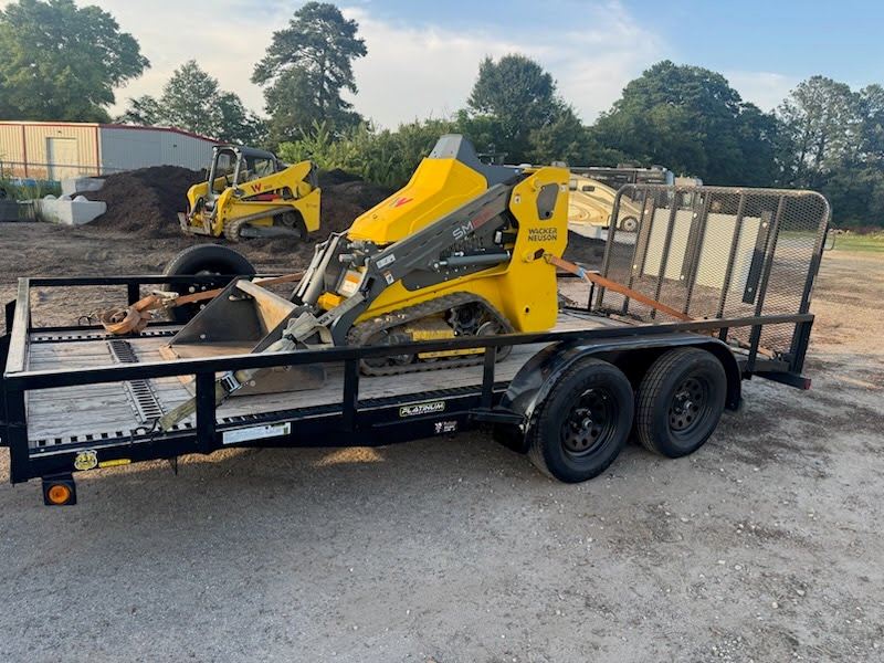 Utility trailer carrying a yellow Wacker Neuson mini skid steer